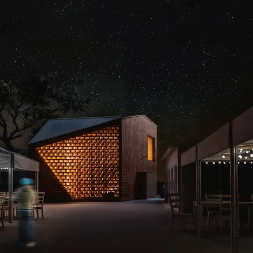 Vista nocturna del proyecto de vivienda con muro de ladrillo iluminado.